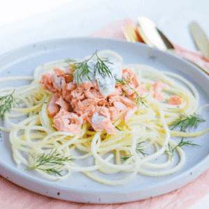 Koolhydraatarme courgetti met warme zalmfilet, gegarneerd met verse dille en een romige saus, geserveerd op een bord