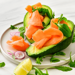 Keto gerookte zalm met avocado op een bord, geserveerd met rucola, veldsla en rode ui, klaar om van te genieten als gezonde lunch.
