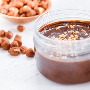 Gezonde keto hazelnoot chocopasta in een glazen pot met hele hazelnoten op de achtergrond