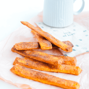 Koolhydraatarme kaneelstengels bestrooid met kaneel geserveerd naast een kop koffie