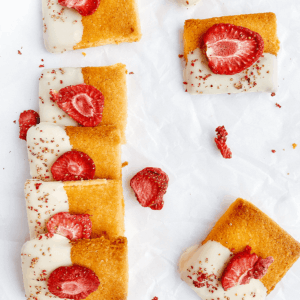 Koolhydraatarme koekjes van amandelmeel met romige topping en verse aardbeien geserveerd op een bord