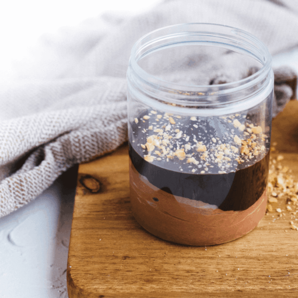 Gezonde chocolademousse in een glazen potje met knapperige toppings op een houten plank