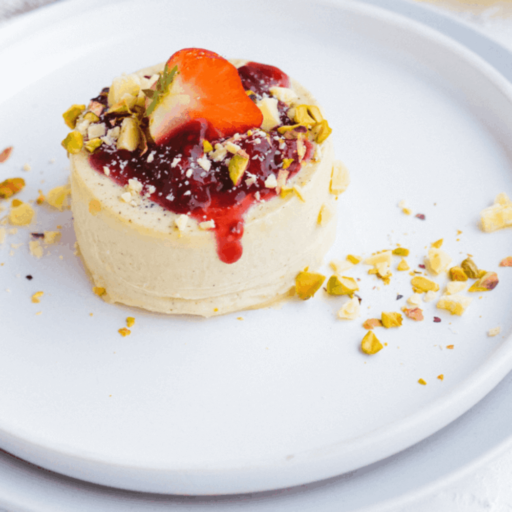 Keto panna cotta met romige structuur en frambozensaus gegarneerd met noten op een wit bord