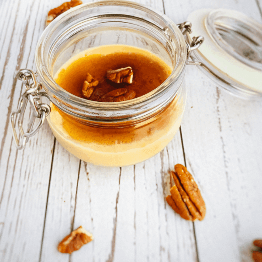 Koolhydraatarme karamelpudding met volle room geserveerd in een glazen potje met noten