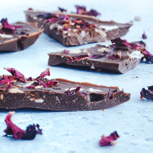 Keto chocolade reep in stukjes gesneden, met krokante granola en gedroogde rozenblaadjes, klaar om van te genieten.