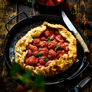 Keto aardbeien galette met een goudbruine amandelmeel bodem gevuld met verse aardbeien geserveerd in een zwarte pan op een rustieke houten tafel