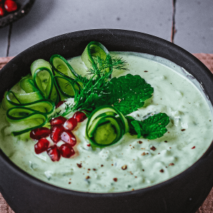 Romige groene avocado tzatziki in een zwarte kom gegarneerd met linten van komkommer verse dille munt granaatappelpitten en een snufje kruiden
