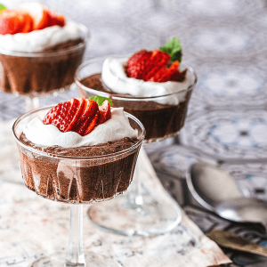 Luchtige keto chocolademousse in glazen met een romige topping en verse aardbeien op een lichte ondergrond.