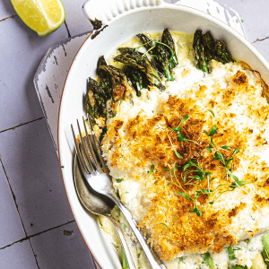 Keto kabeljauw met knapperig kokoslaagje geserveerd met groene asperges en romige saus op een wit bord