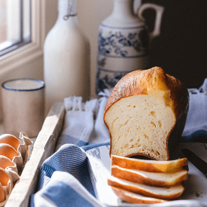 Luchtig keto brioche brood in plakjes gesneden geserveerd op een doek met eieren en melk op de achtergrond