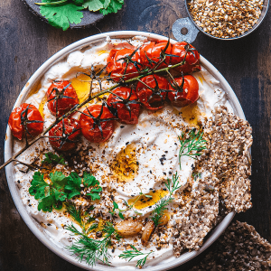 Romige labneh van Griekse yoghurt met geroosterde trostomaten olijfolie verse kruiden en zaden crackers op een schaal