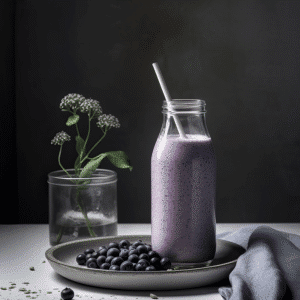 Koolhydraatarme bosbessen smoothie in een glazen fles met rietje geserveerd op een schaal met verse bosbessen en een zachte paarse kleur