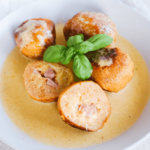 Meerdere goudbruine Cordon bleu-balletjes in een romige gele saus, gegarneerd met verse basilicum — een heerlijke koolhydraatarme en keto-vriendelijke variant van het klassieke ham-en-kaasgerecht voor gezond eten en gewichtsverlies