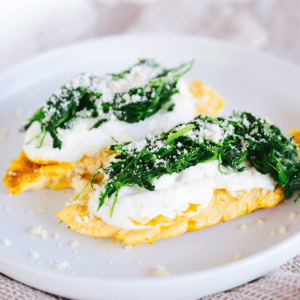 Een wit bord met twee luchtige goudbruine omeletten belegd met gebakken spinazie, romige fetakaas en geraspte Parmezaan, geserveerd als een gezond koolhydraatarm keto ontbijt voor gewichtsverlies en een gezond dieet.
