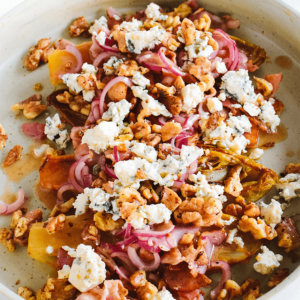 Een rustieke salade met plakjes geroosterde gele bieten, verkruimelde blauwe kaas, dunne rode uien en gehakte walnoten, met dressing op de bodem als een koolhydraatarme en gezonde maaltijd voor uw dieet.