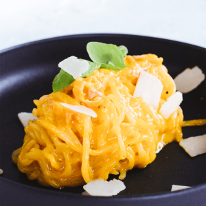 Een bord romige spaghetti carbonara op een zwart bord, bedekt met een rijke oranjegele saus en gegarneerd met Parmezaanse vlokken en verse basilicum — een koolhydraatarme, keto-vriendelijke variant van de klassieke Italiaanse pasta voor een gezond dieet en gewichtsverlies.