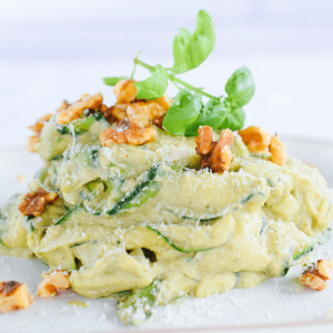 Een bord courgettenoedels gemengd met romige groene pestosaus, gegarneerd met hele walnoten, geraspte Parmezaanse kaas en verse basilicum — een heerlijke, koolhydraatarme en keto-vriendelijke pastavariant voor een gezond dieet en gewichtsverlies.