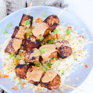 Keto vegan tempeh saté met pindasaus, geserveerd op bloemkoolrijst en gegarneerd met gehakte lente uitjes. Een heerlijke, koolhydraatarme en keto vriendelijke vegetarische maaltijd voor een gezond dieet en gewichtsverlies.