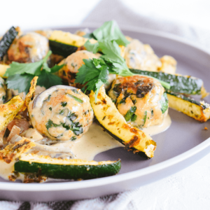 Een grijs bord met gekruide gehaktballetjes en courgetteschijfjes in een romige saus, gegarneerd met verse kruiden — een smakelijke, koolhydraatarme en keto-vriendelijke maaltijd voor een gezond dieet en gewichtsverlies.