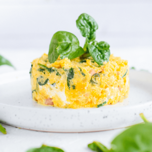 Een kleine cilindervormige soufflé van spinazie en zalm met een gele eierbasis, gegarneerd met verse spinazieblaadjes op een wit gespikkeld bord, een gezond koolhydraatarm en keto-vriendelijk gerecht voor gewichtsverlies en een gezonde levensstijl.