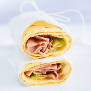 Twee eiwraps gevuld met plakjes ham en avocado, samengebonden met keukentouw op een bord — een handige koolhydraatarme keto maaltijd voor ontbijt of lunch, ideaal voor gezond dieet en gewichtsverlies