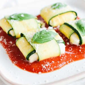 Een bord met keto courgette ravioli, gemaakt van dunne plakjes courgette gevuld met romige ricotta, geserveerd op een rijke tomatensaus en gegarneerd met geraspte Parmezaanse kaas en verse basilicum — een heerlijke koolhydraatarme maaltijd voor gezond dieet en gewichtsverlies.