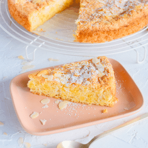 Een plakje vochtige amandelmeel cake op een roze bord, getopt met geschaafde amandelen en poedersuiker, een koolhydraatarm en keto vriendelijk dessert voor gezond eten en gewichtsverlies.