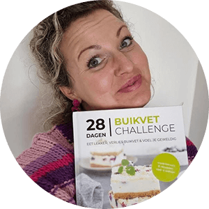 Een glimlachende vrouw houdt het kookboek "28 Dagen Buikvet Challenge" van Gezonderecepten.nl vast, met op de cover een gelaagd no-bake dessert met romige vulling en rode bessen — een vriendelijk portret ter promotie van de koolhydraatarme gids voor gewichtsverlies