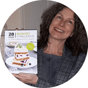 Een persoon houdt het Nederlandse hardcover kookboek "28 Dagen Buikvet Challenge," met op de cover een gelaagd dessert met romige vulling en rode bessen, met een koolhydraatarm dieetplan voor gewichtsverlies en het aanpakken van buikvet — een tevreden klant van Gezonderecepten.nl.