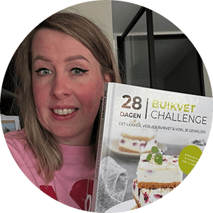 Een persoon houdt het Nederlandse kookboek "28 Dagen Buikvet Challenge," met op de cover een gelaagd no-bake dessert met romige vulling en rode bessen, met koolhydraatarme recepten, maaltijdplannen en boodschappenlijsten voor gewichtsverlies en het aanpakken van buikvet — een tevreden klant van Gezonderecepten.nl.