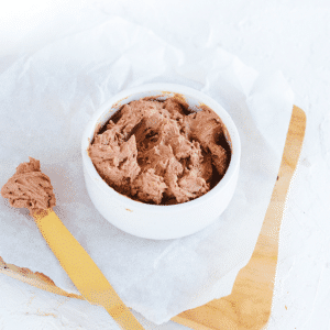 Een kom met romige chocolade cottage cheese mousse met een gele spatel op bakpapier ernaast, klaar om te serveren als koolhydraatarme keto dessert- of smeersel voor fruit en toast — rijk aan proteïne en ideaal voor gezond dieet en gewichtsverlies.