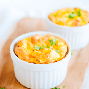 Twee goudgele gebakken eisoeflés in witte keramische ramekins, gegarneerd met verse groene kruiden, geplaatst op een houten oppervlak — een lichte en luchtige koolhydraatarme keto ontbijt- of brunchmaaltijd ideaal voor gezond dieet en gewichtsverlies.