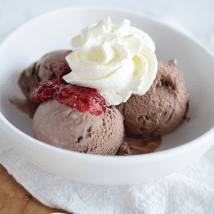 Drie bolletjes chocolade kwarkijs in een witte kom, getopt met slagroom en frambozensaus, een romig koolhydraatarm en keto-vriendelijk dessert voor gezond eten en gewichtsverlies.