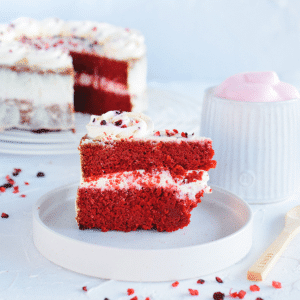 Een plak rode fluweelcake met felrode lagen en dikke witte roomkaasglazuur op een wit bord, een koolhydraatarm en keto vriendelijk dessert ideaal voor gezond eten en gewichtsverlies.