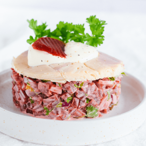 Een netjes gelaagde tartaar van rode biet en forel op een wit bord, met onderaan romige biet en kruiden, in het midden lichte vis en bovenop een witte yoghurtsaus met roodbruine purée en een takje peterselie — een levendige koolhydraatarme keto maaltijd van Gezonderecepten.nl, ideaal voor gezond dieet en gewichtsverlies.