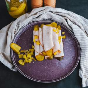 Vleesrolletjes gevuld met gesneden augurken, gegarneerd met gehakte augurken, geserveerd op een paarse schaal met een augurkenpot en kruidenmolens op de achtergrond, ideaal voor keto, low-carb en afvallen