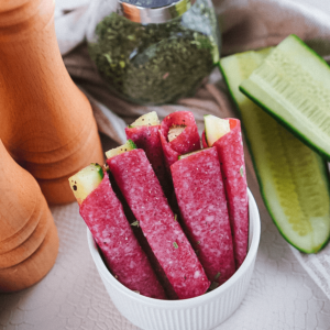 Wit kommetje gevuld met salamirolletjes met roomkaas en komkommer, met een houten pepermolen en een potje gedroogde kruiden op de achtergrond, ideaal voor afvallen en gezond dieet