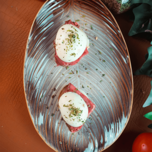 Twee halve hardgekookte eieren geserveerd op een plak gerookt vlees, bestrooid met gedroogde kruiden, op een bladvormig bord — een keto en koolhydraatarme snack voor gewichtsverlies en gezond dieet.