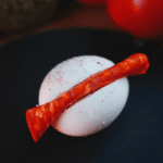 Hardgekookt ei met een plakje roodgedroogde worst erop, bestrooid met zwarte peper — een eenvoudige keto en koolhydraatarme appetizer voor gewichtsverlies en gezond dieet