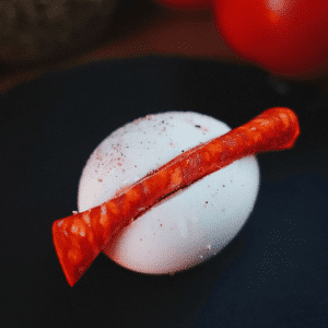 Hardgekookt ei met een plakje roodgedroogde worst erop, bestrooid met zwarte peper — een eenvoudige keto en koolhydraatarme appetizer voor gewichtsverlies en gezond dieet