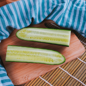 Twee komkommerhelften op een houten snijplank, met het witte vruchtvlees en de zaden zichtbaar, met een blauw-wit gestreepte doek op de achtergrond, ideaal voor gezonde low-carb gerechten