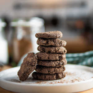 Stapel van zeven donkere chocoladekoekjes met een rustieke gebarsten textuur op een wit bord, kruimels eromheen, ideaal voor low-carb, keto en gezond dieet.