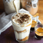 Een hoog glas tiramisu iced coffee met lagen romige vulling, met koffie doordrenkte lange vingers en een bovenlaag met cacaopoeder, geserveerd met espresso shots, geschikt voor keto-, low-carb- en gewichtsverliesvriendelijk dieet.