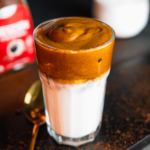 Een glas Dalgona koffie met melk onderaan en luchtige opgeklopte koffieschuim bovenop, een keto- en low-carb vriendelijke drank geschikt voor gezond dieet en gewichtsverlies.