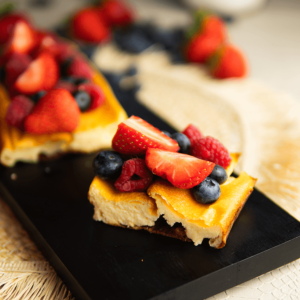 Twee stukken luchtige en romige yoghurtcake, gegarneerd met verse aardbeien, blauwe bessen en frambozen op een zwart serveerbord, ideaal voor keto-, low-carb- en gezond dieet.