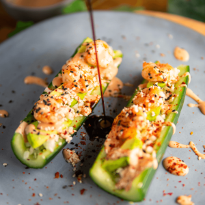 Twee komkommerhelften gevuld met een romige garnalen en avocadomix, gegarneerd met sesamzaad en sauzen. Ideaal voor keto, lowcarb en gezond dieet.