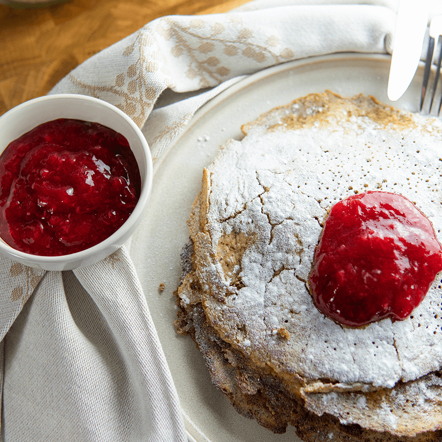 Stapel low-carb pannenkoeken op een wit bord, gegarneerd met frambozensaus, met een klein kommetje extra saus ernaast, ideaal voor keto en low-carb dieet.