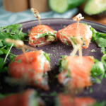 Gerookte zalmrolletjes gevuld met roomkaas en avocado, geserveerd op een bedje van rucola en gegarneerd met verse kruiden, een perfecte keto-vriendelijke en low-carb appetizer voor een gezond dieet