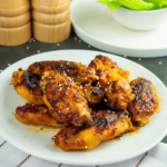 Een bord met airfryer-buffalo kippenvleugels geglazuurd met een hartige saus en bestrooid met sesamzaad, geserveerd met selderijsticks — een heerlijk koolhydraatarm gerecht voor gezond afvallen en diëten