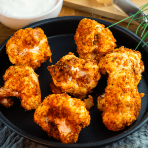 Een pan met krokante airfryer-bloemkoolroosjes in een pittige korst, geserveerd met een kom dipsaus, een smakelijk koolhydraatarm gerecht voor gewichtsverlies en een gezond dieet